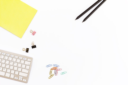 Computer Keyboard, A Yellow Pad, Two Black Pencil And Clips For Paper On White Background. Minimal Concept Workplace At The Office.