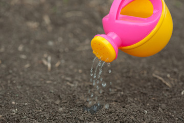 A pink yellow watering can water the ground. Drops of water spill, dissipate moisturize the earth. Help fight the drought.