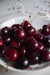 Cherries close-up on a white plate with a pattern and on a white tablecloth. Vertical arrangement.