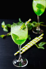 Green alcoholic or non-alcoholic refreshing summer cocktail, mojito, sparkling drink with mint and ice in a beautiful glass on a dark wooden background 