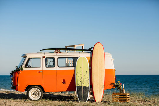 bus with a surfboard on the roof is a parked near the beach © boykovi1991