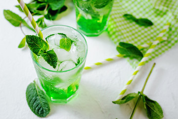 Green alcoholic or non-alcoholic refreshing summer cocktail, mojito, sparkling drink with mint and ice in a traditional glass on a white rustic background 