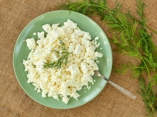 Cheese in green plate on linen background with sprig of seasoning.