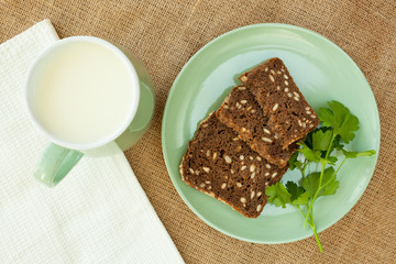 Milk in green cup on linen background with pieces bread.