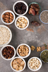 Above view of ingredients for homemade granola, oats, different nuts and raisins, dates, seed on the grey stone background, selective focus