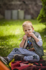 Fototapeta premium Young cute boy eating a piece of meat in a park on a picnic
