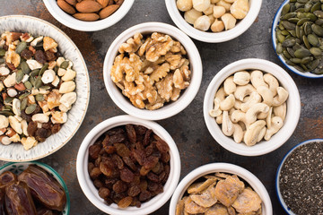 Ingredients for homemade paleo granola, different nuts and raisins, dates, seed on the grey stone background, top view