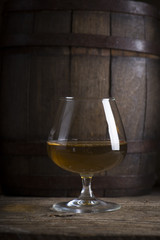 Glass of Cognac and old oak barrel defocussed