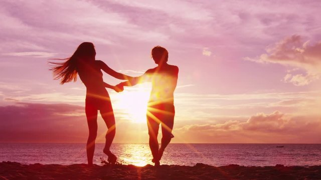 Romantic couple dancing on beach having fun at sunset playful and happy on honeymoon travel travel vacation holiday. Happy joyful lovers swirling around together.