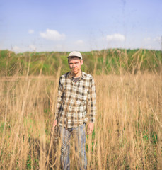 Naklejka na ściany i meble A hipster man in a plaid shirt stands in a dry tall grass