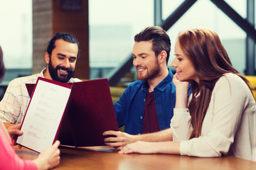 smiling friends discussing menu at restaurant