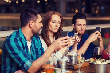 friends with smartphones dining at restaurant