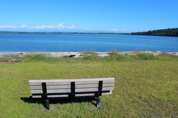 Naklejka na ściany i meble An empty bench with a beautiful bay view waiting for someone to sit and relax 