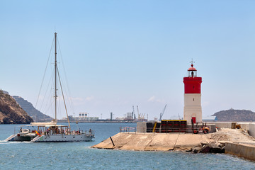 Fototapeta na wymiar Cartagena, Spain - July 13, 2016: A pleasure boat sails along the mediterranean sea next to the lighthouse.
