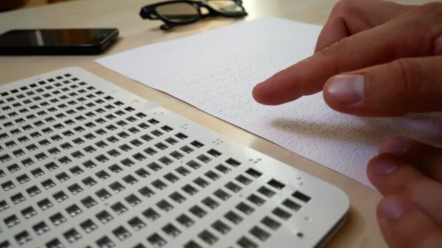 Blind Man Reading Braille. Blind Manager or Businessman in the Workplace behind the Desk Reading Braille. Man learns to read Braille on a Sheet of Paper Sitting at the Desk in Office. Read Braille