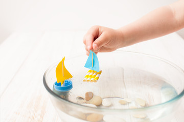 Child's hand holds small boat, playing in kitchen