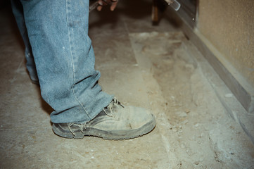 Building construction site and feet of a worker wearing boots on gray dusty concrete background
