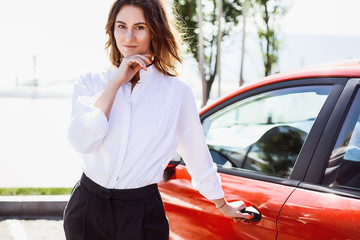 Fototapeta premium Business lady standing with car, woman in white shirt, success,happy, curly hair, manager
