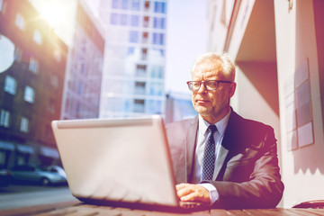 senior businessman with laptop at city street cafe