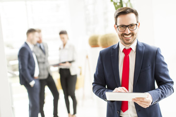 Businessman working on a tablet while other young business people talking in the background