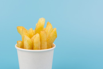 close up of french fries in a paper cup on blue background