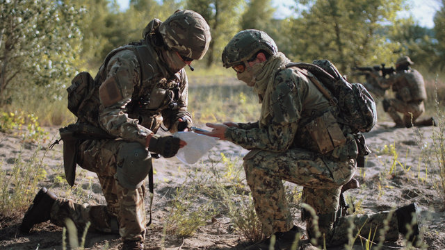 Two soldiers sitting in nature and using map and gps tracker for navigation.