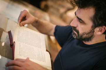 Naklejka premium Curious man reading old book in his library at home
