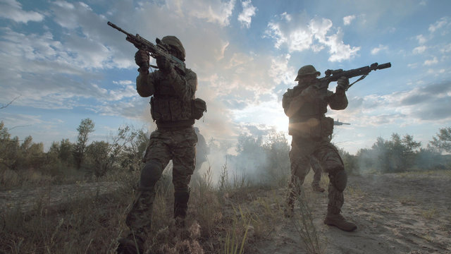 Silhouettes of soldiers walking on battlefield and aiming with guns.