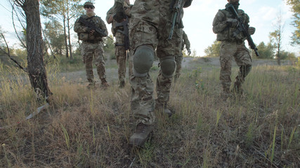 Unrecognizable military people with firearms walking on battlefield.
