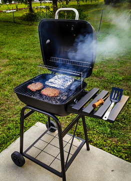 Garden portable BBQ cooking burgers and foil wrapped beans