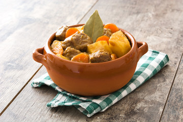Beef meat stewed with potatoes, carrots and spices in ceramic bowl on wooden table
