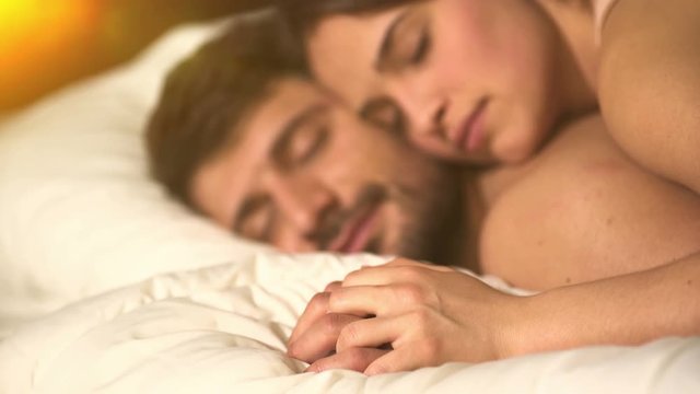 The happy couple lay on the bed and hold hands. close up