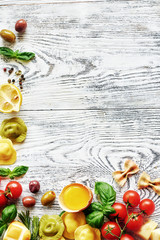 Fresh ingredients for italian lunch or dinner: uncooked tortellini, pasta, raw egg, cheese, tomato, basil and olives, lemon and pepper on white table. Food frame with copy space.