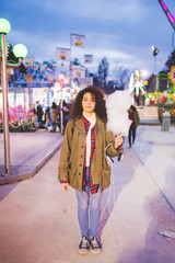 Young beautiful mixed race woman outdoor in a lunapark in the night posing with cotton candy - sweet, snack, childhood concept