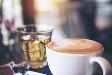 Closeup image of a cup of hot coffee and a tea glass on vintage wooden table in cafe