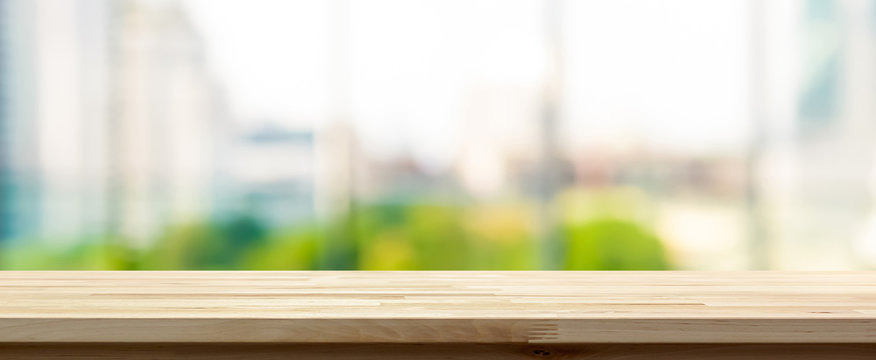 Wood table top on blur  city building view background looking through glass window, panoramic banner