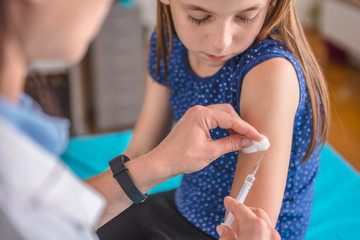 Doctor giving a young girl a vaccine shot - obrazy, fototapety, plakaty