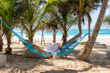 Naklejka na ściany i meble Junge Frau liegt in einer Hängematte unter Palmen am Strand der Karibik