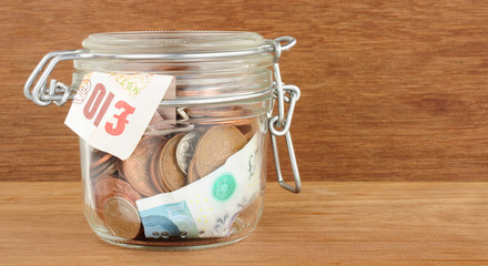 Glass jar filled with cash savings on a wood background © philip kinsey