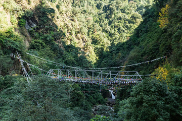 Tibetan Buddhist Prayer Flag include red, green, yellow, blue and white colors swaddle bridge and trees in Sikkim, India.