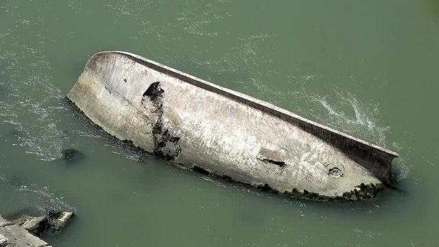 Footage of capsized boat crashed onto rocks in middle of fresh green colored river water flowing around the wreck from which only the bottom starboard side is shown in 4k high resolution quality