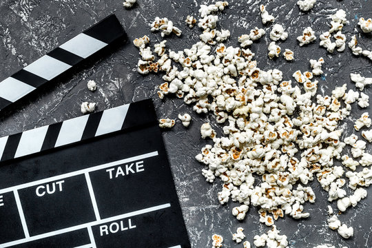 Watching the film. Movie clapperboard and popcorn on grey stone table background top view
