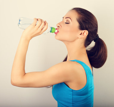 Beautiful happy sporty slim woman holding and drinking water from the bottle. Closeup portrait. Toned