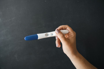 Pregnancy test in a girl's hand, against a black chalkboard background. The concept of pregnancy.