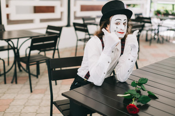 Emotional male mime artist sitting and posing at the table in a restaurant.