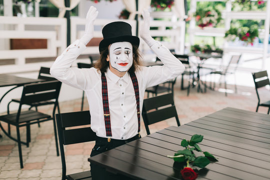 Emotional male mime artist sitting and posing at the table in a restaurant.