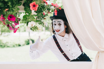 Pantomime theater artist posing near the pot of summer flowers.
