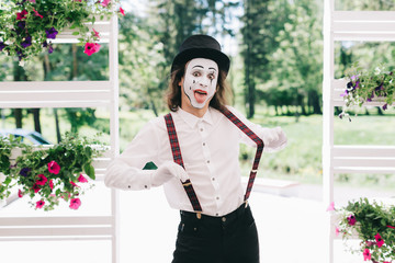 Pantomime theater artist posing near the pot of summer flowers.