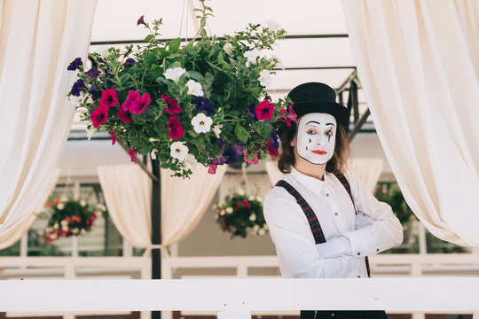 Pantomime theater artist posing near the pot of summer flowers.