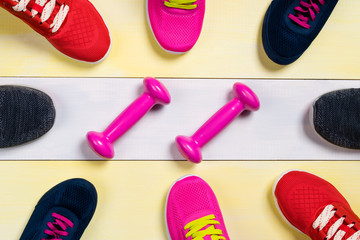 Scattered sports shoes on a multi-colored floor, in the middle lies a set of sports dumbbells